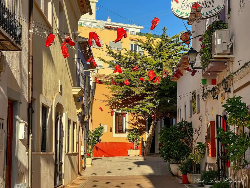 Sunny restaurant lane decorated with red shoes in Calpe Old Town